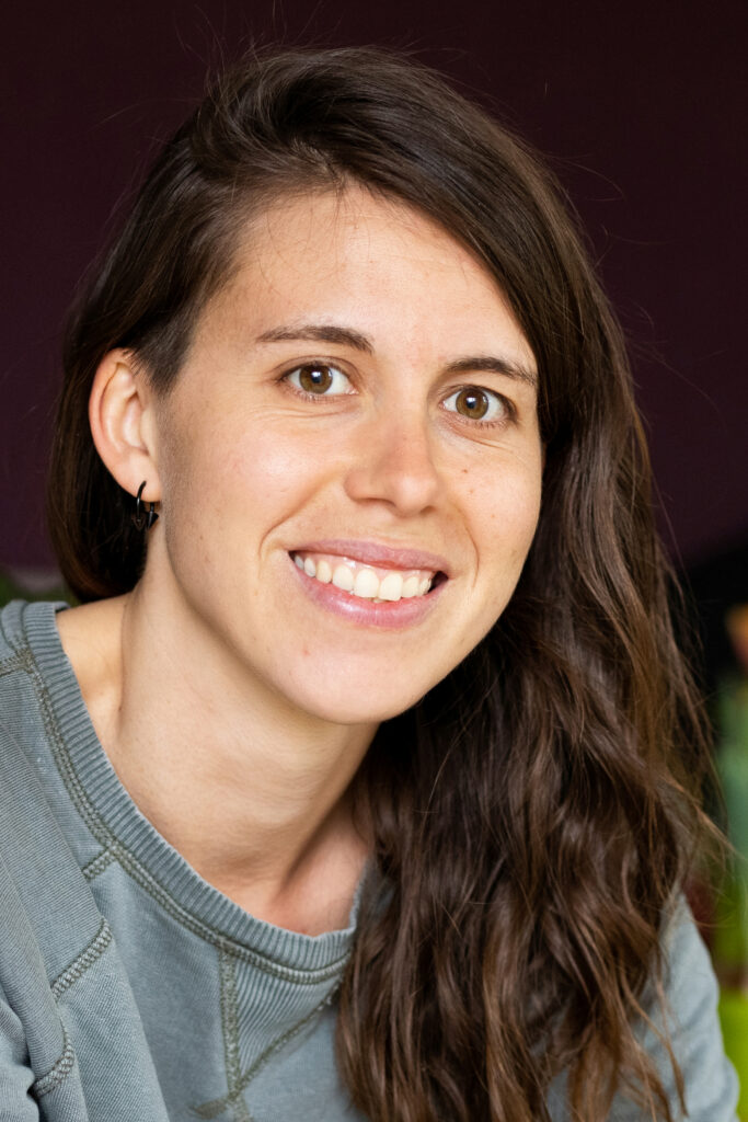A portrait of Léïla Eisner. Léïla is smiling in front of a dark background.
